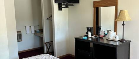 A hotel room with a bed, a dresser, a television mounted on the wall, a mirror, a lamp, and a coffee maker.