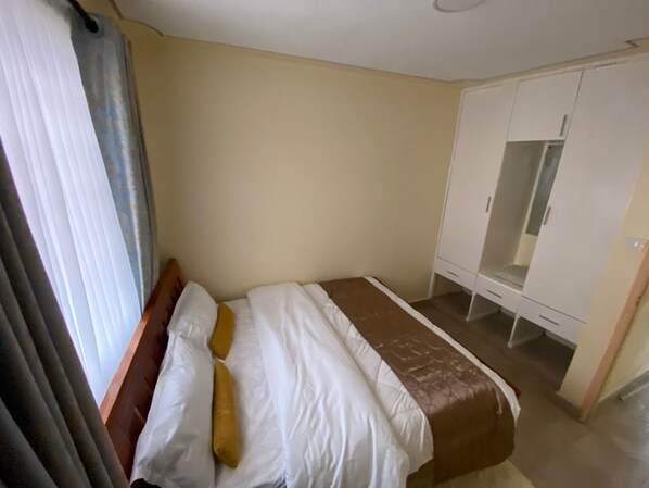 A bedroom with a bed, a wardrobe, and a window with curtains.