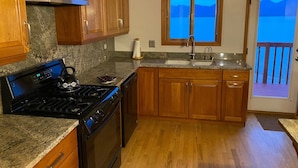 A kitchen with wooden cabinets, a granite countertop, a stove, a sink, and a window with a view of the outdoors.