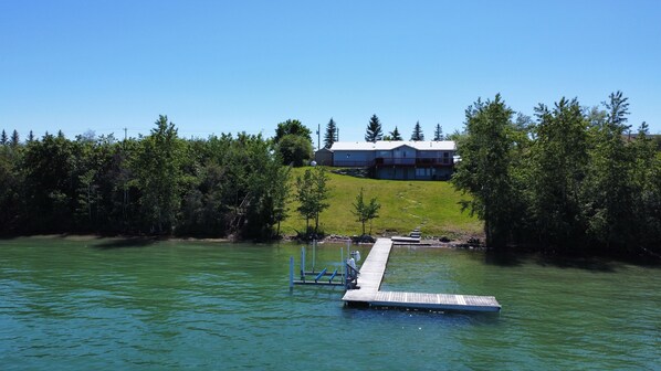 A dock extending into a lake with a house in the background surrounded by trees.