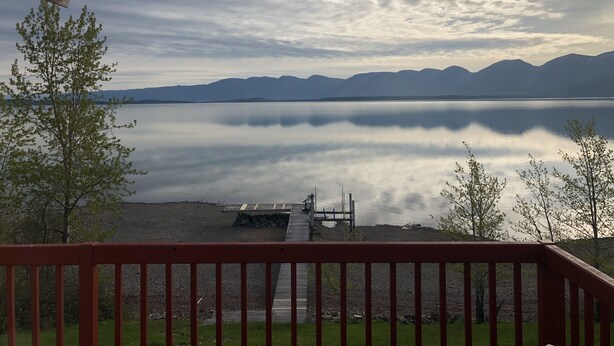 A lake with mountains in the background, a dock, and a red railing.