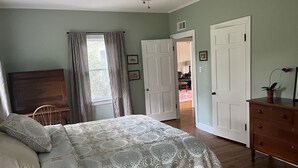 Un dormitorio con cama, cómoda de madera, ventilador de techo y puerta que da a otra habitación.