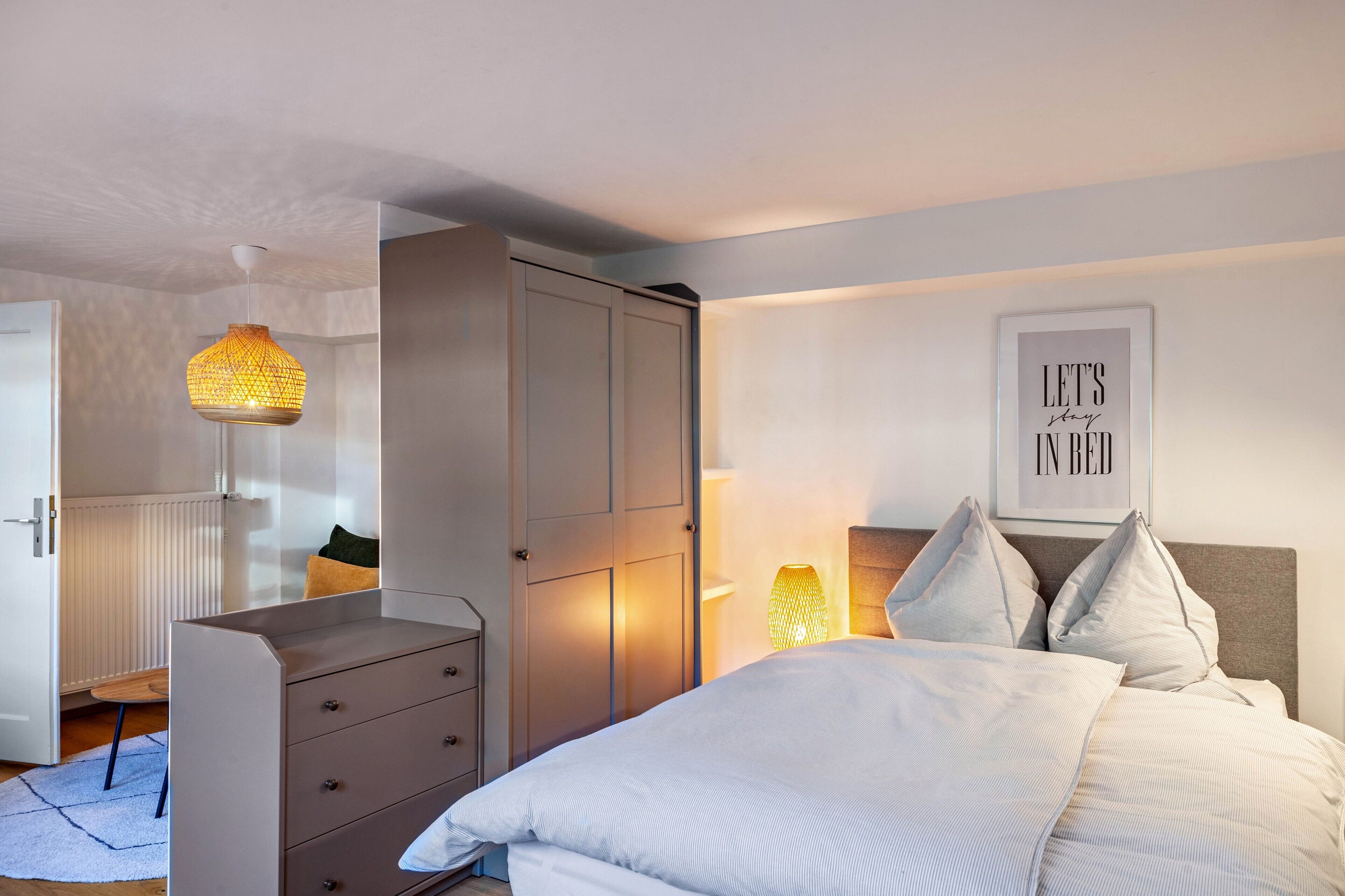Un dormitorio con cama, cómoda, armario, lámpara de pared y una cita enmarcada.