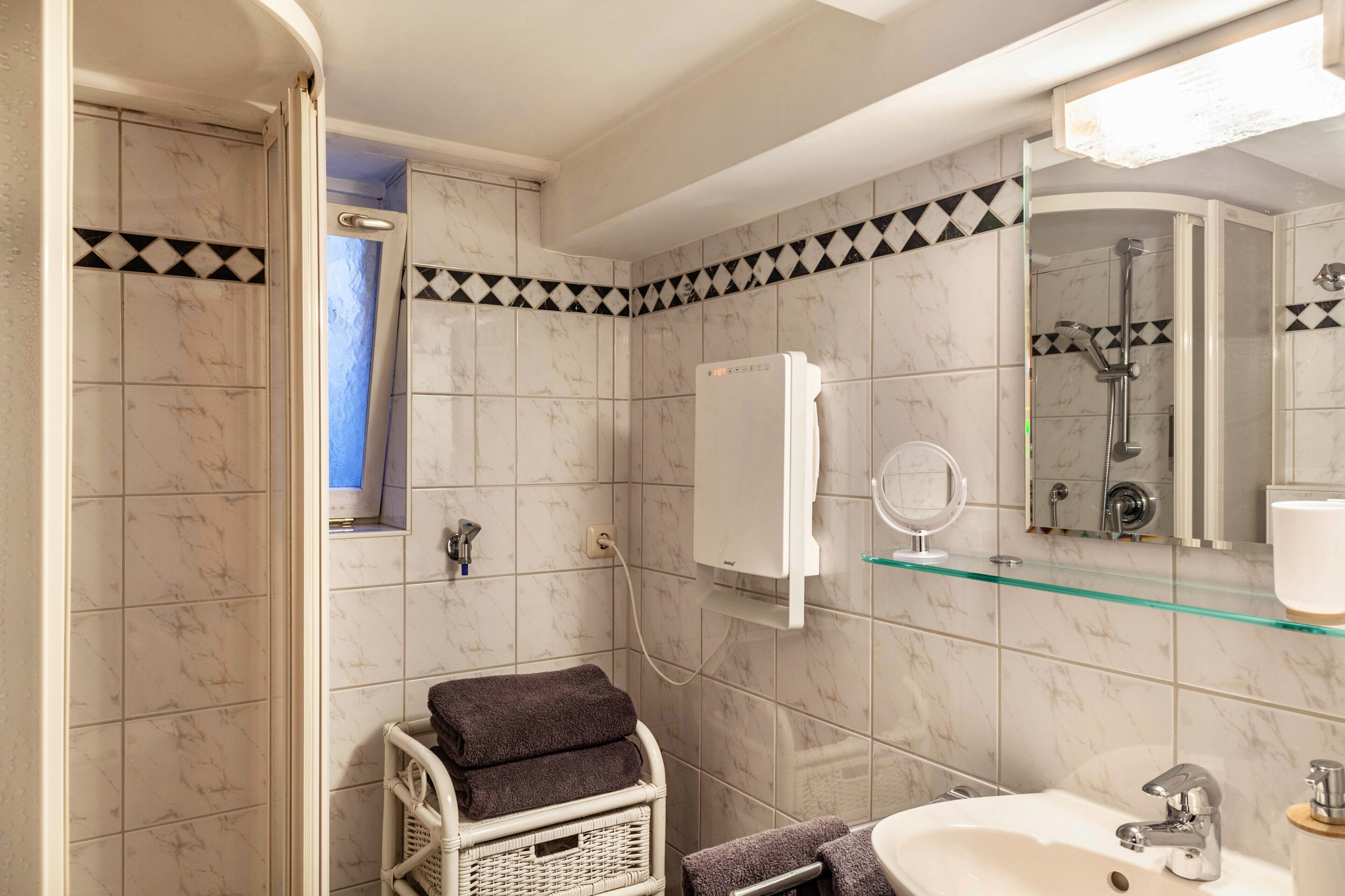A bathroom with a shower, a sink, a mirror, and a glass shelf.