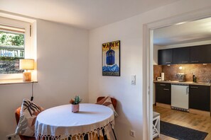 Una cocina compacta con armarios oscuros, un refrigerador pequeño y una zona de comedor con una mesa redonda y sillas.