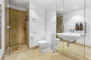 A modern bathroom with a glass-enclosed shower, a white toilet, and a large mirror above a sink. - Elegant stunning marina views (Auckland)