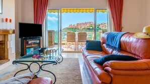 A living room with a sofa, a glass coffee table, a TV, and a balcony with a view of buildings. - View Of The Sun Apartment With Pool, Mijas Costa, Spain (Mijas Costa)
