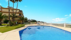 A swimming pool with a white fence, palm trees, and a building in the background. - View Of The Sun Apartment With Pool, Mijas Costa, Spain (Mijas Costa)