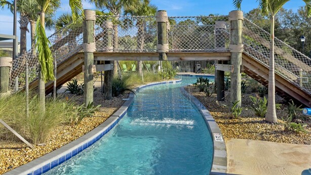 A pool area with a water slide, palm trees, and a wooden bridge.