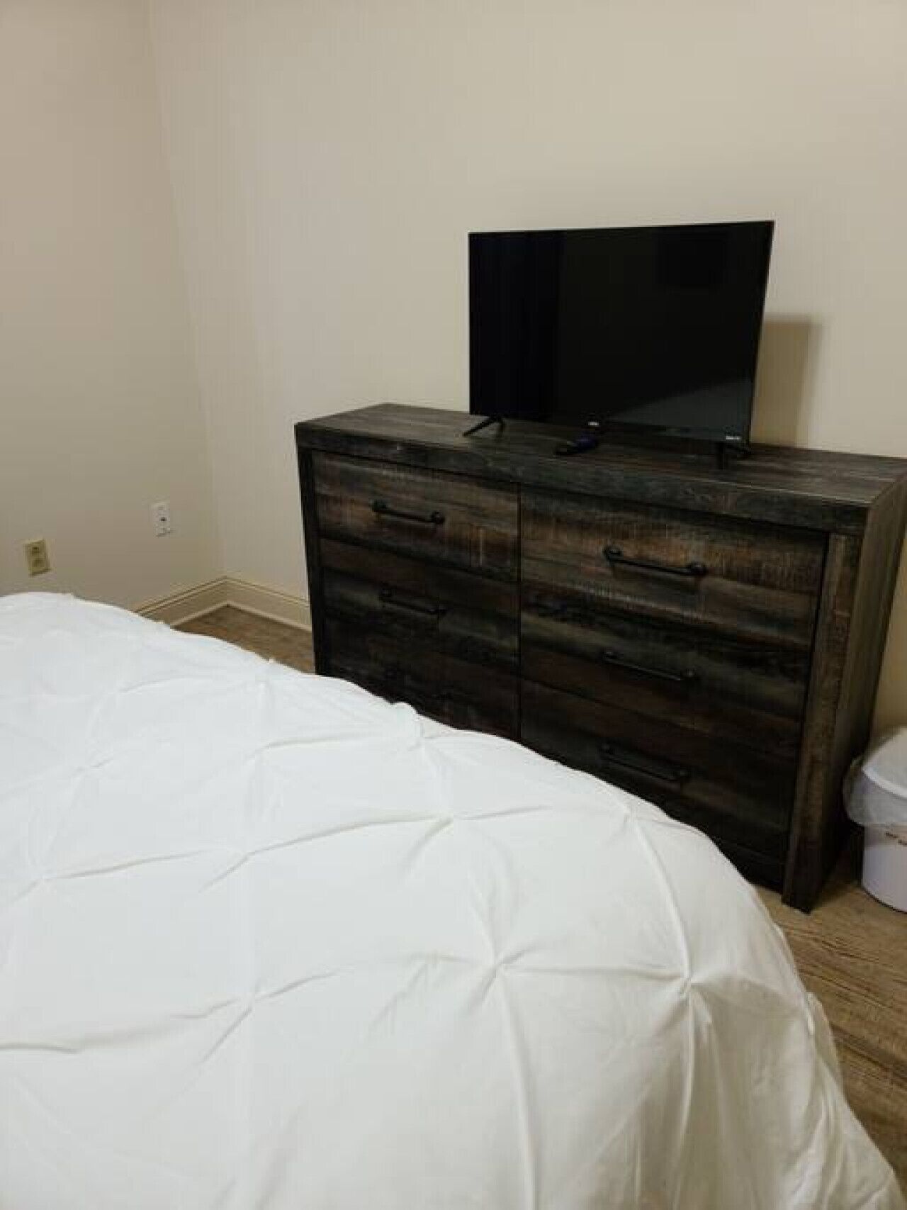 A bedroom with a bed, a dresser, and a television on top of the dresser.
