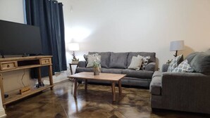 Uma sala de estar com um sofá cinza, uma mesa de centro de madeira e uma televisão sobre um suporte de madeira.