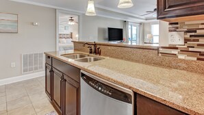 A modern kitchen with granite countertops, stainless steel appliances, and pendant lighting. - Tybee Getaway Just Steps to the Beach! (Tybee Island)