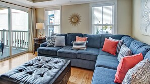 A living room with a sectional sofa, a tufted ottoman, and a sunburst wall decoration. - Tybee Getaway Just Steps to the Beach! (Tybee Island)