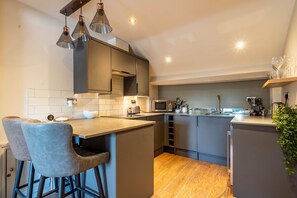 A modern kitchen with a central island, bar stools, a microwave, and a coffee machine.