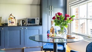 Una cucina moderna con mobili blu scuro, un tavolo da pranzo con piano in vetro e vista sulla città attraverso un'ampia finestra.