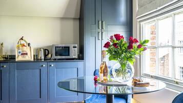 A modern kitchen with dark blue cabinets, a glass-top dining table, and a view of the city through a large window.