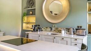 Una cucina moderna con piano cottura integrato, lavello e specchio rotondo. Si vedono scaffali con oggetti decorativi e una macchina da caffè.