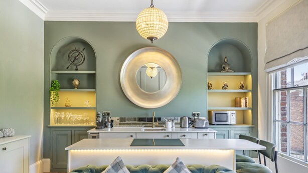 Una cucina moderna con isola centrale, illuminazione a sospensione e scaffalature integrate.