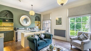Una cucina moderna con isola centrale, zona pranzo con divano e poltrona, e un'ampia finestra vista verde.