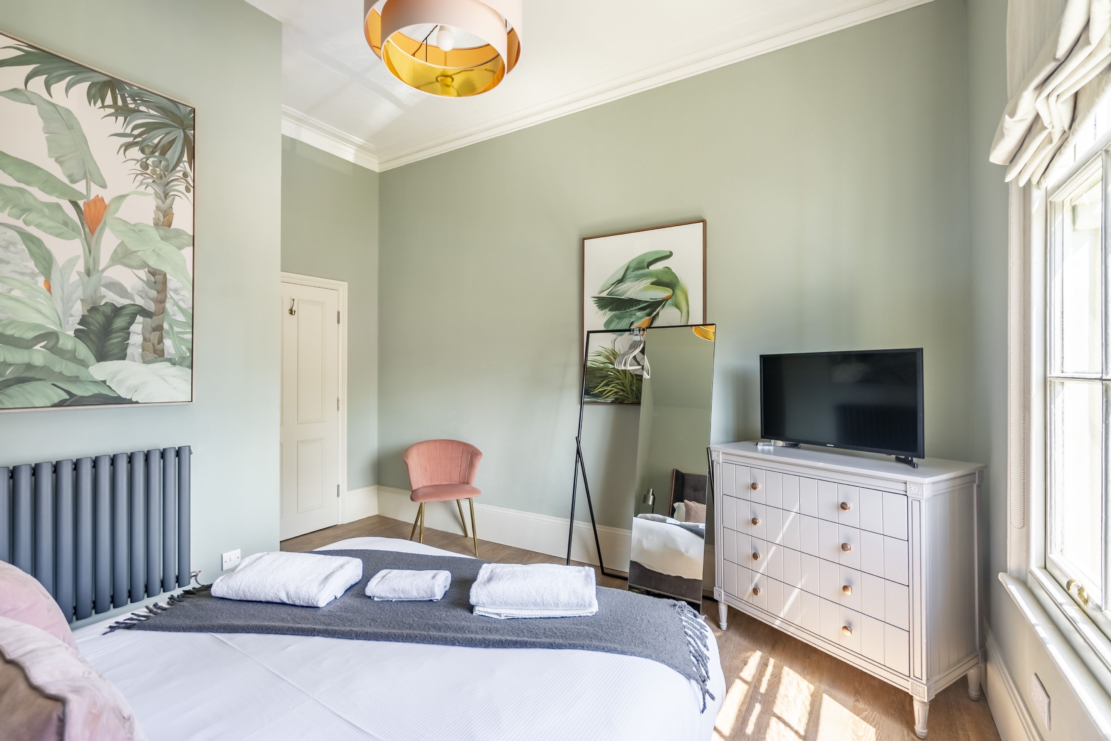 A bedroom with a bed, a dresser, a television, a chair, and artwork on the walls.