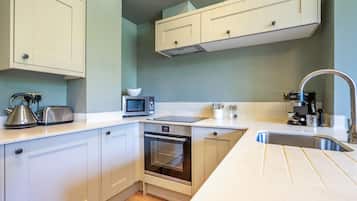 A compact kitchen with white cabinets, a microwave, a kettle, a coffee machine, and a stainless steel sink.