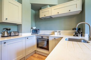 A compact kitchen with white cabinets, a microwave, a kettle, a coffee machine, and a stainless steel sink.