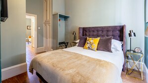 A bedroom with a large bed, a bedside table with a lamp, a wall-mounted TV, and a door leading to another room. - A premium stay that sleeps 2 guests  in 1 bedroom (York)