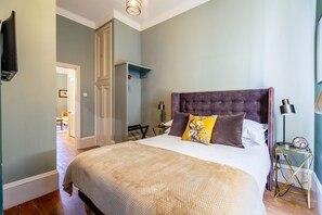 Una camera da letto con un letto grande, un comodino con una lampada, una TV a parete e una porta che dà su un'altra stanza.