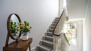 A staircase with a wooden handrail and carpeted steps, a wooden console table with a mirror and potted plants, and a window with a view of the outdoors.