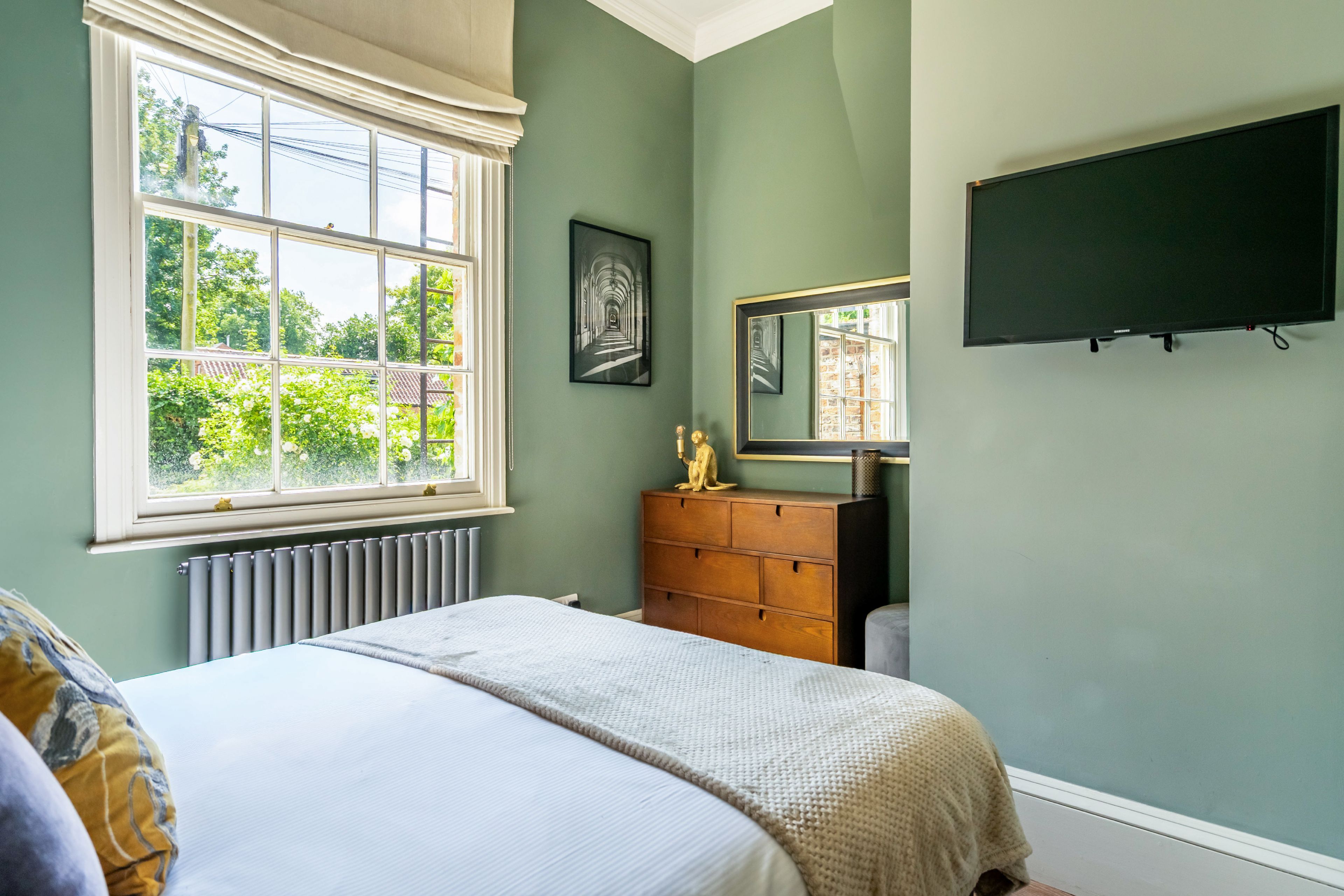 A bedroom with a bed, dresser, and a large window.