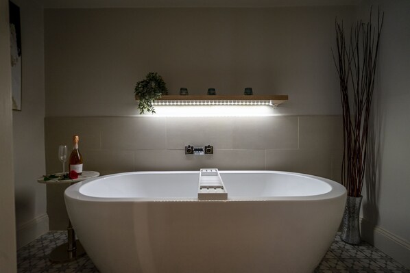 A modern bathroom with a freestanding bathtub, a shelf with decorative items, and a wall-mounted light fixture. - A couples retreat that sleeps 2 guests  in 1 bedroom (York)