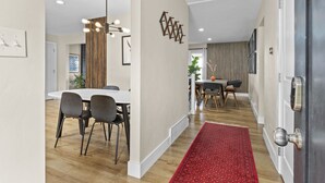 A modern dining area with a white table and chairs, a red rug leading to a door, and a wall-mounted light fixture. - 5BR Mountainside Home w/ Views - Near SLC, Park City & Lagoon (Bountiful)