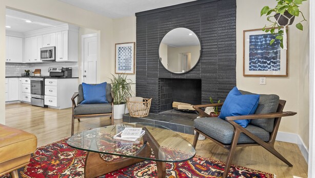 A modern living room with a glass coffee table, two grey armchairs, a black fireplace, and a kitchen in the background. - 5BR Mountainside Home w/ Views - Near SLC, Park City & Lagoon (Bountiful)