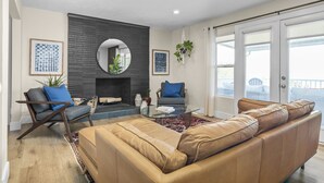 A modern living room with a leather sofa, a glass coffee table, and two armchairs. There is a fireplace, a large mirror, and a view of the outdoors through a sliding glass door. - 5BR Mountainside Home w/ Views - Near SLC, Park City & Lagoon (Bountiful)