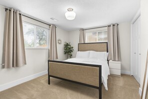 A bedroom with a bed, a nightstand, a window with curtains, a ceiling light, and a radiator. - 5BR Mountainside Home w/ Views - Near SLC, Park City & Lagoon (Bountiful)
