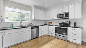 A modern kitchen with white cabinets, stainless steel appliances, and a wooden floor. - 5BR Mountainside Home w/ Views - Near SLC, Park City & Lagoon (Bountiful)