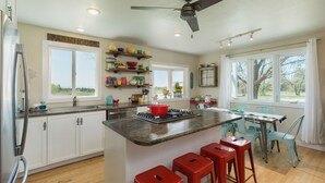 A modern kitchen with white cabinets, a central island with stools, a refrigerator, and a dining area with chairs and a table. - Charming retreat close to downtown, hiking, lakes, 3 acre and private (Durango)