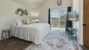 A bedroom with a bed, a ceiling fan, a mounted deer head, a wall-mounted TV, and a view through a large window. - Charming retreat close to downtown, hiking, lakes, 3 acre and private (Durango)