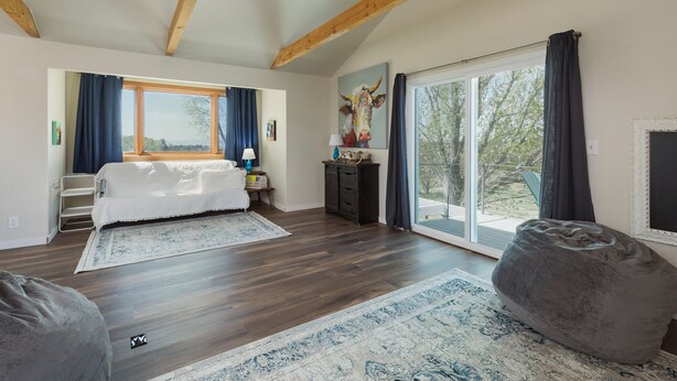 A spacious room with a large bed, a bean bag, a wooden floor, a large window, and a sliding glass door. - Charming retreat close to downtown, hiking, lakes, 3 acre and private (Durango)