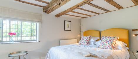 Un dormitorio con una cama, una ventana con flores, un radiador y una mesita.