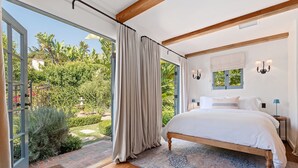 Een slaapkamer met een groot bed, houten vloeren, een kamerbreed tapijt en uitzicht op een tuin door een schuifdeur van glas.