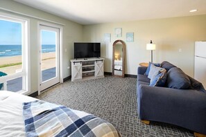 A hotel room with a bed, a sofa, a TV, a mirror, and a view of the beach.