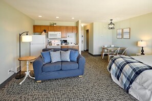 A compact hotel room with a kitchenette, a sofa, a bed, and a dining table.