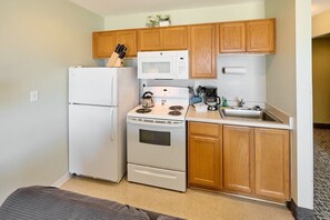 A compact kitchen with a refrigerator, microwave, stove, and sink.