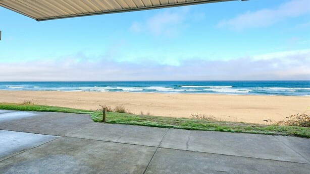 A beach view from a covered patio with a concrete floor and a metal roof.