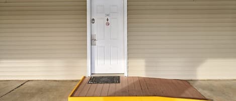 A white door with a no entry sign, a ramp leading to a yellow curb, and a blue parking space.