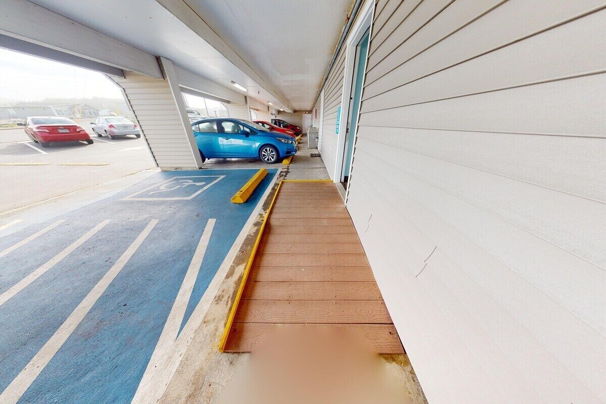 Un estacionamiento con una rampa que lleva a una puerta de garaje, un espacio reservado para discapacitados de color azul, y varios coches estacionados adentro.