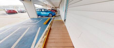 Un estacionamiento con una rampa que lleva a una puerta de garaje, un espacio reservado para discapacitados de color azul, y varios coches estacionados adentro.