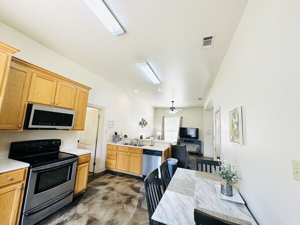 A kitchen with wooden cabinets, a microwave, stove, and a dishwasher. There is a dining area with a table and chairs.