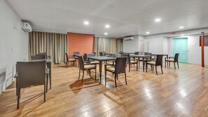 Um quarto amplo, com várias mesas e cadeiras, parede de tijolos e porta com moldura azul clara.